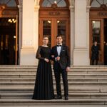 Elegantný pár pred operou večer v čiernom oblečení na schodoch so zlatým svetlom