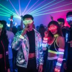 Mladí ľudia na techno párty v neónovom oblečení s LED doplnkami, laserové svetlá, tanečný parket.