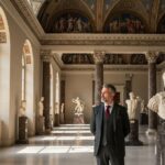 Interiér klasickej galérie s mramorovými plastikami a kurátorom v historickom oblečení