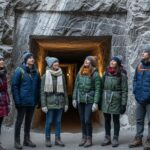 skupina turistov v teplom oblečení pri vstupe do soľnej bane Wieliczka s kamennými stenami