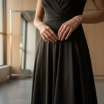 Osoba upravuje čierne hodvábne šaty v minimalistickej šatni s prirodzeným svetlom.